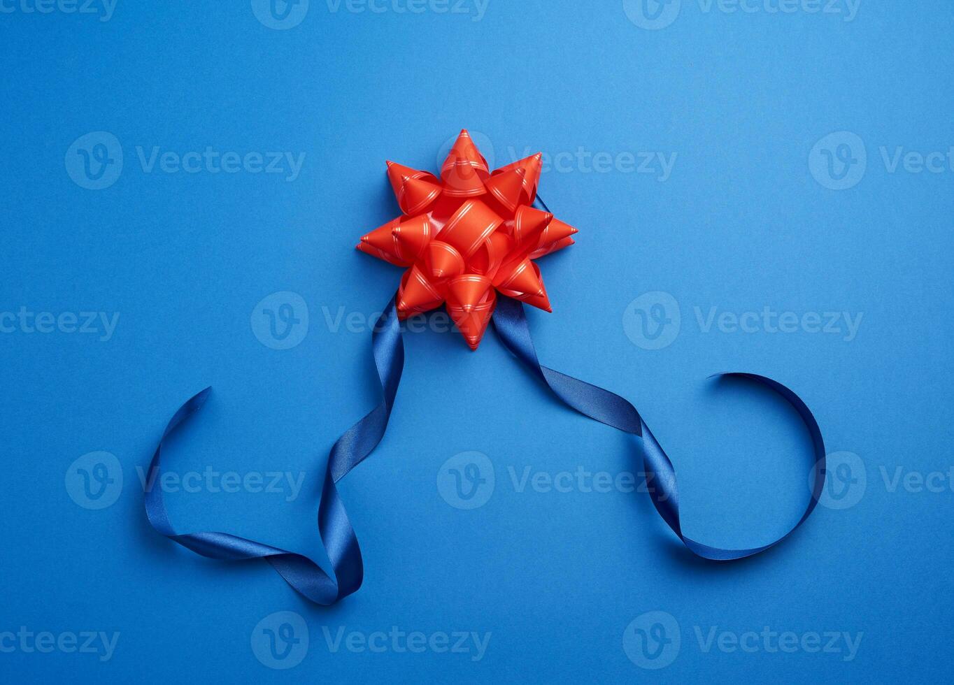 cinta delgada de seda azul retorcida y lazo rojo brillante sobre un fondo azul foto