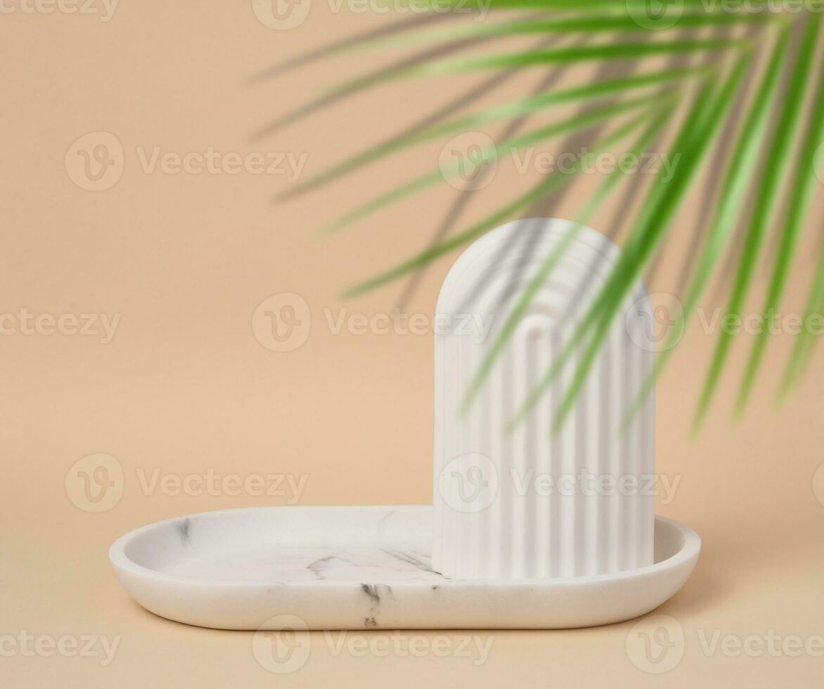 Empty oval white marble stand on a beige background and a shadow from palm leaves, a place to display cosmetics and products photo
