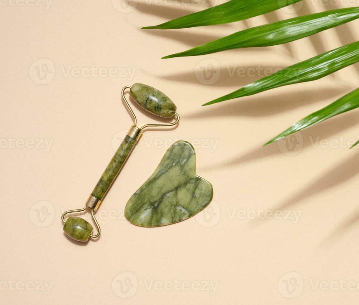 Green jade gouache massager and massage jade roller on a beige background, top view photo