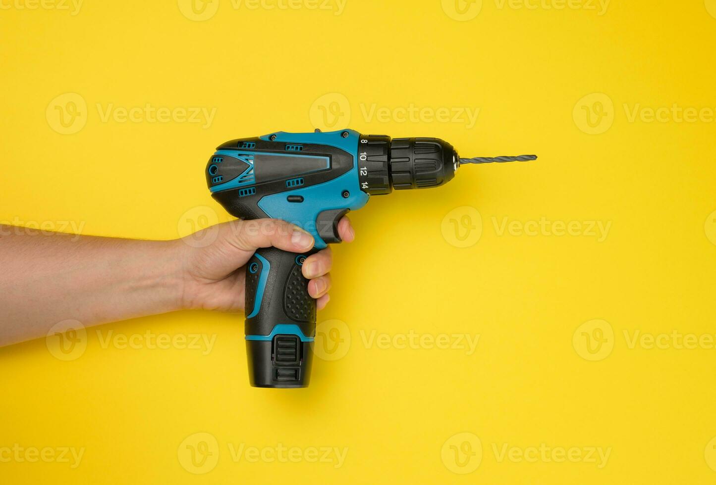 female hand holds a cordless drill on a yellow background. Tool for work photo