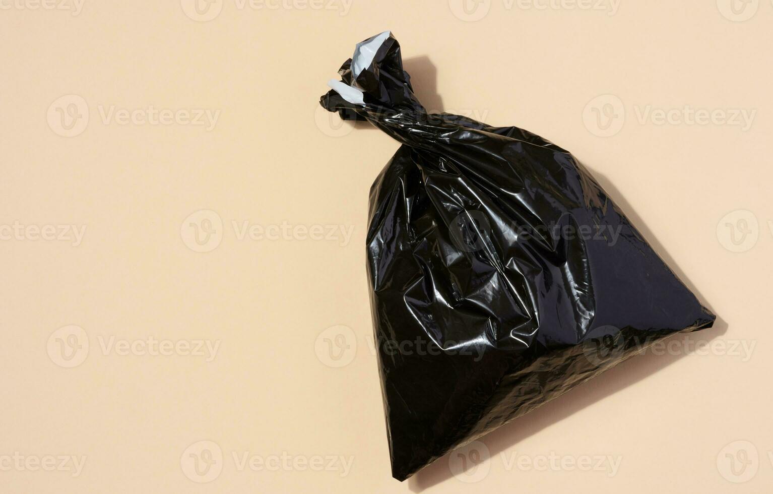 Full black plastic bag on a beige background, top view photo
