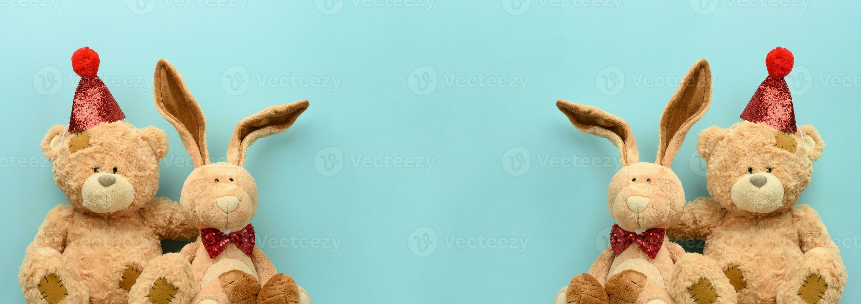 Teddy bear in a festive cap and a plush hare on a blue background. Festive background photo