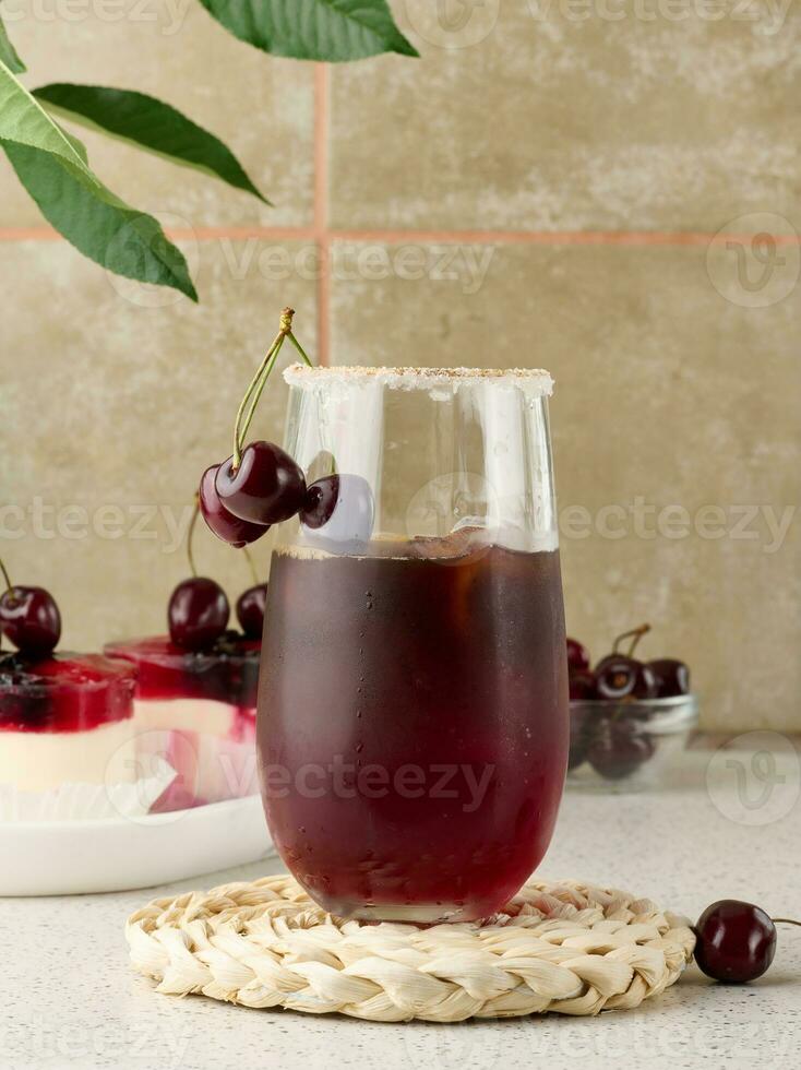Cherry juice in a transparent glass and fresh cherries on a white table photo