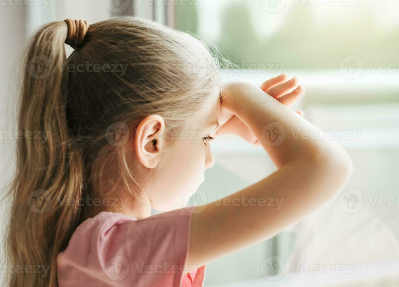 Sad little girl looking through  window at home. photo