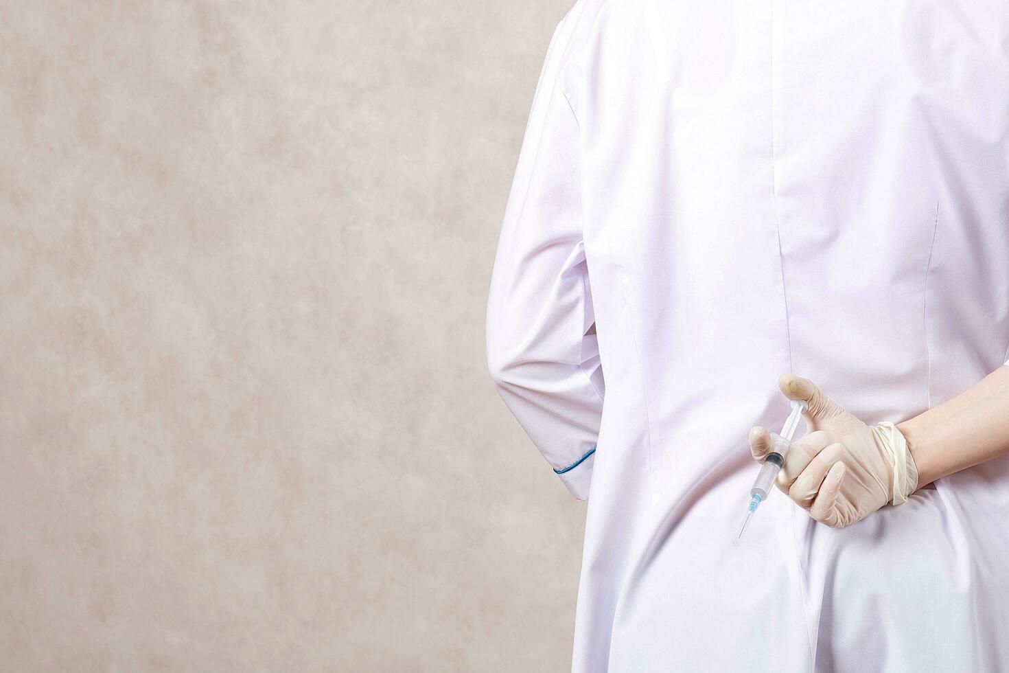 A doctor dressed in a professional uniform hides syringe with medication photo