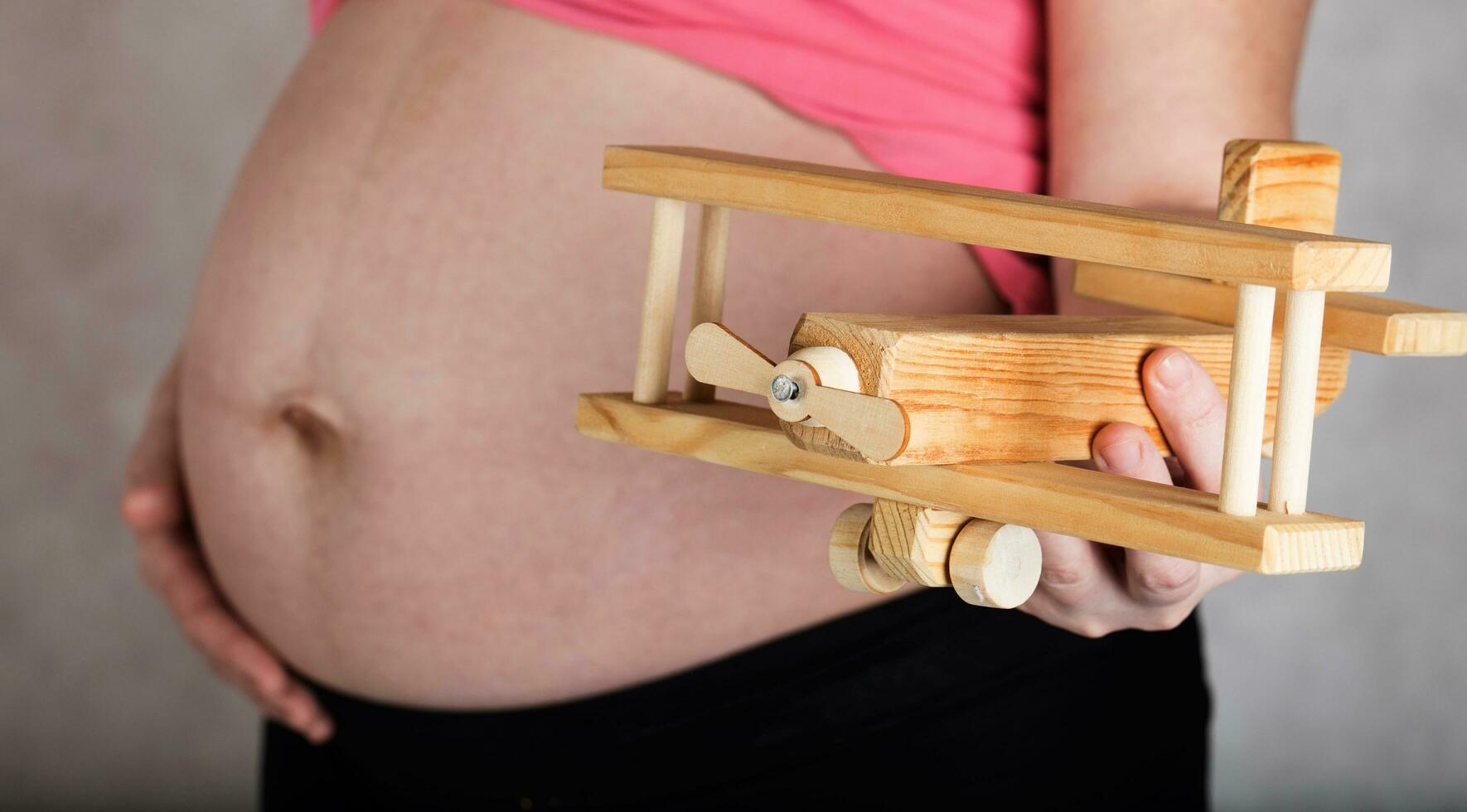 joven embarazada mujer mantiene de madera hecho avión. foto