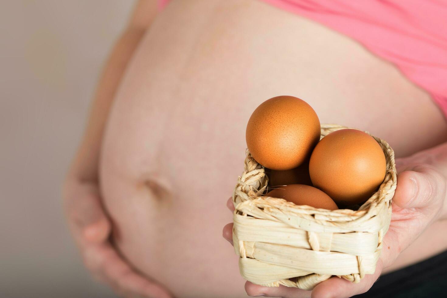Young pregnant woman keeps woven mini basket with chicken eggs. photo