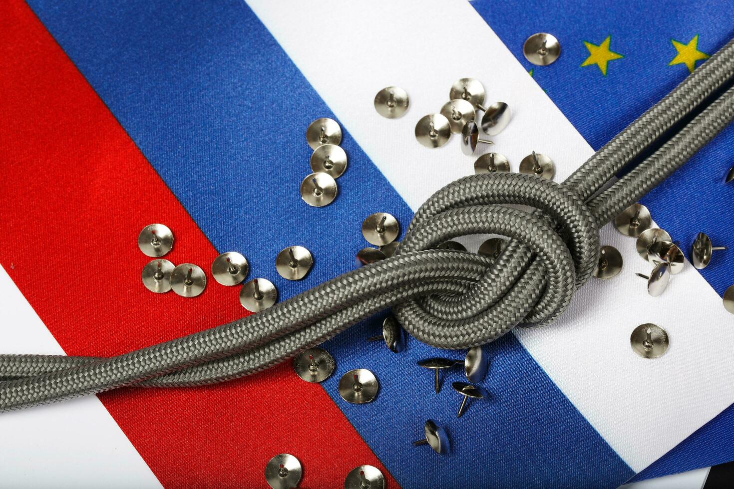 Rope with a knot and pins on flags of EU and Russia. Background photo