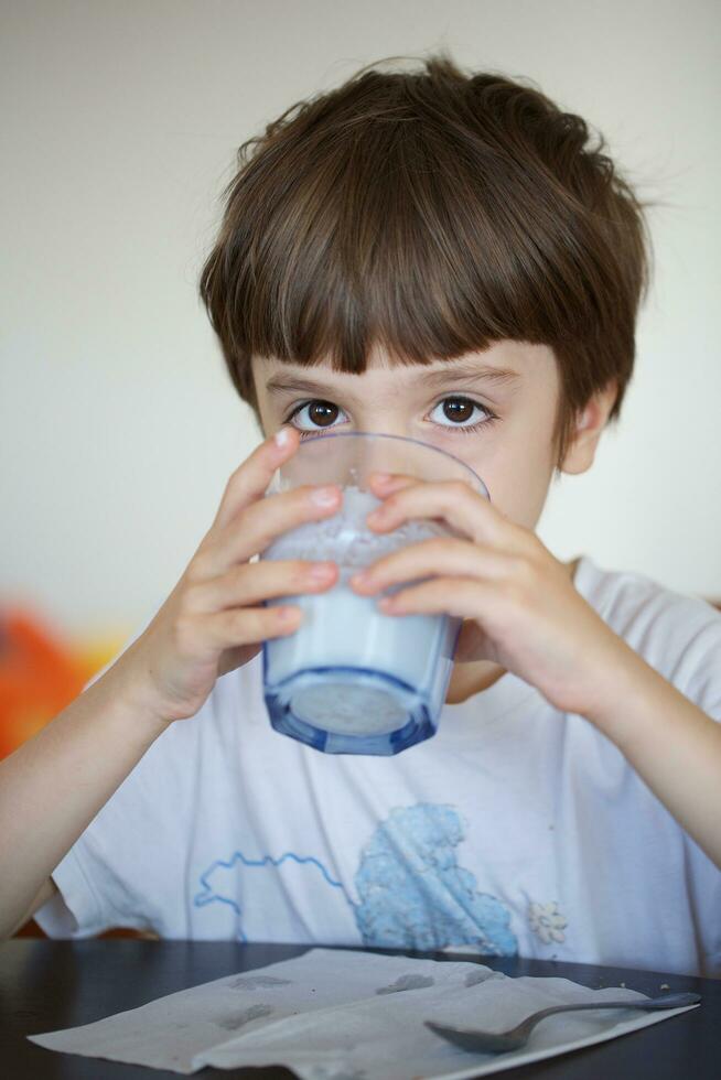 Boy of six years is taking a glass of warm milk with oat biscuits. photo