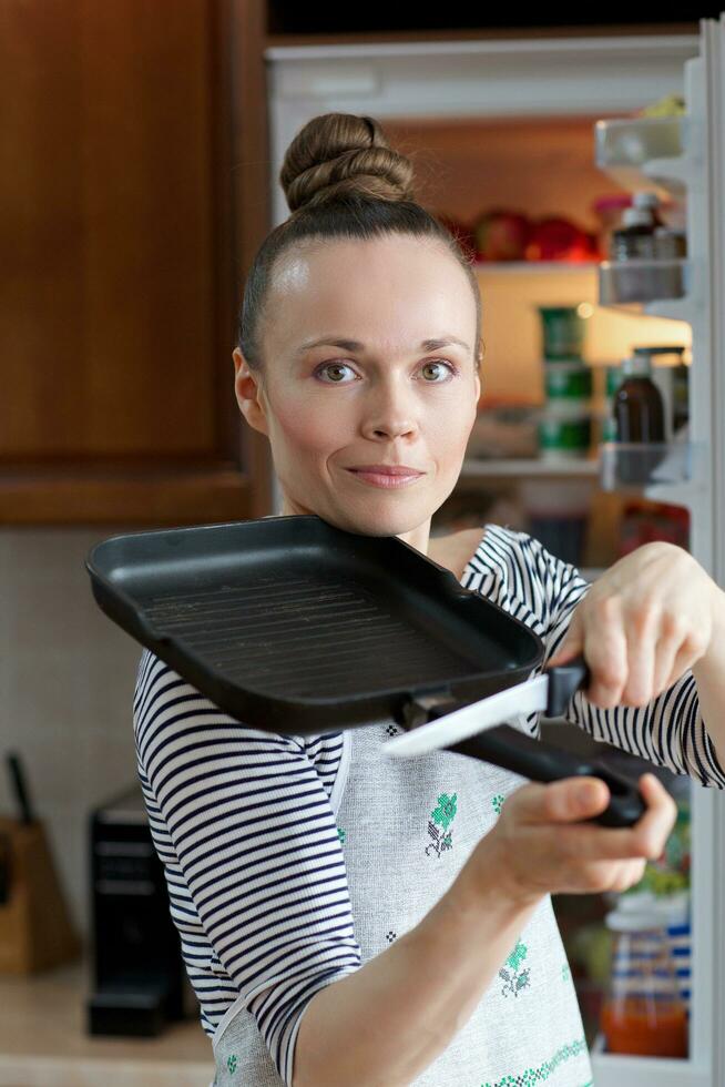 Young lady between is staying in front of the fridge. photo