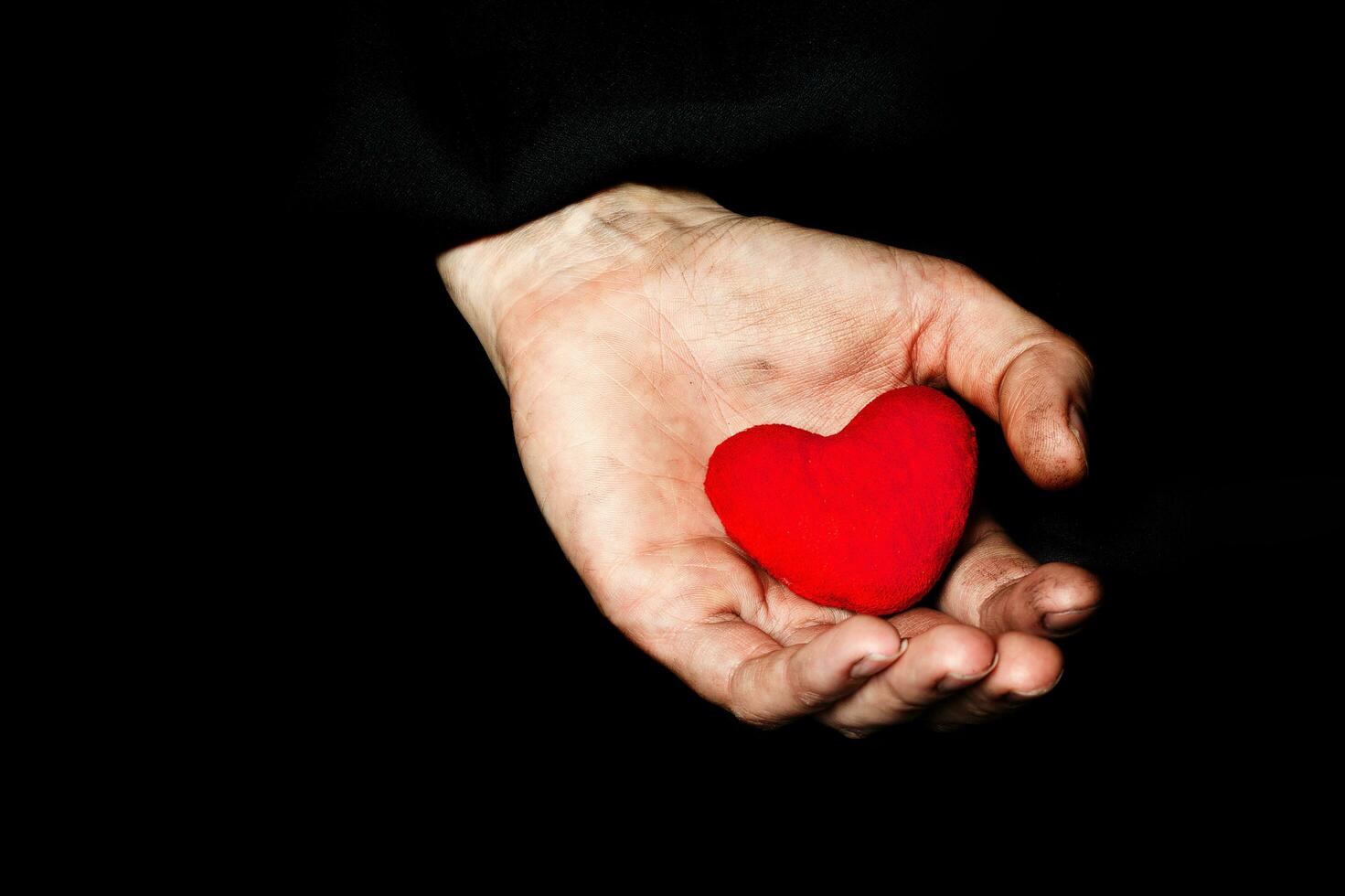 Palm of a peasant woman with plush red heart on a black fabric. photo