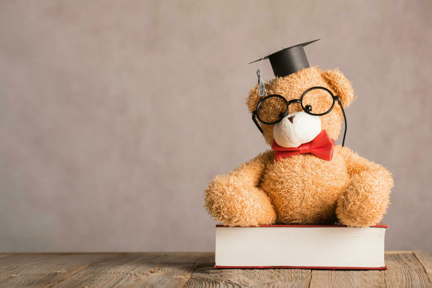 Brown teddy bear in an academic cap is placed on a thick dictionary. photo