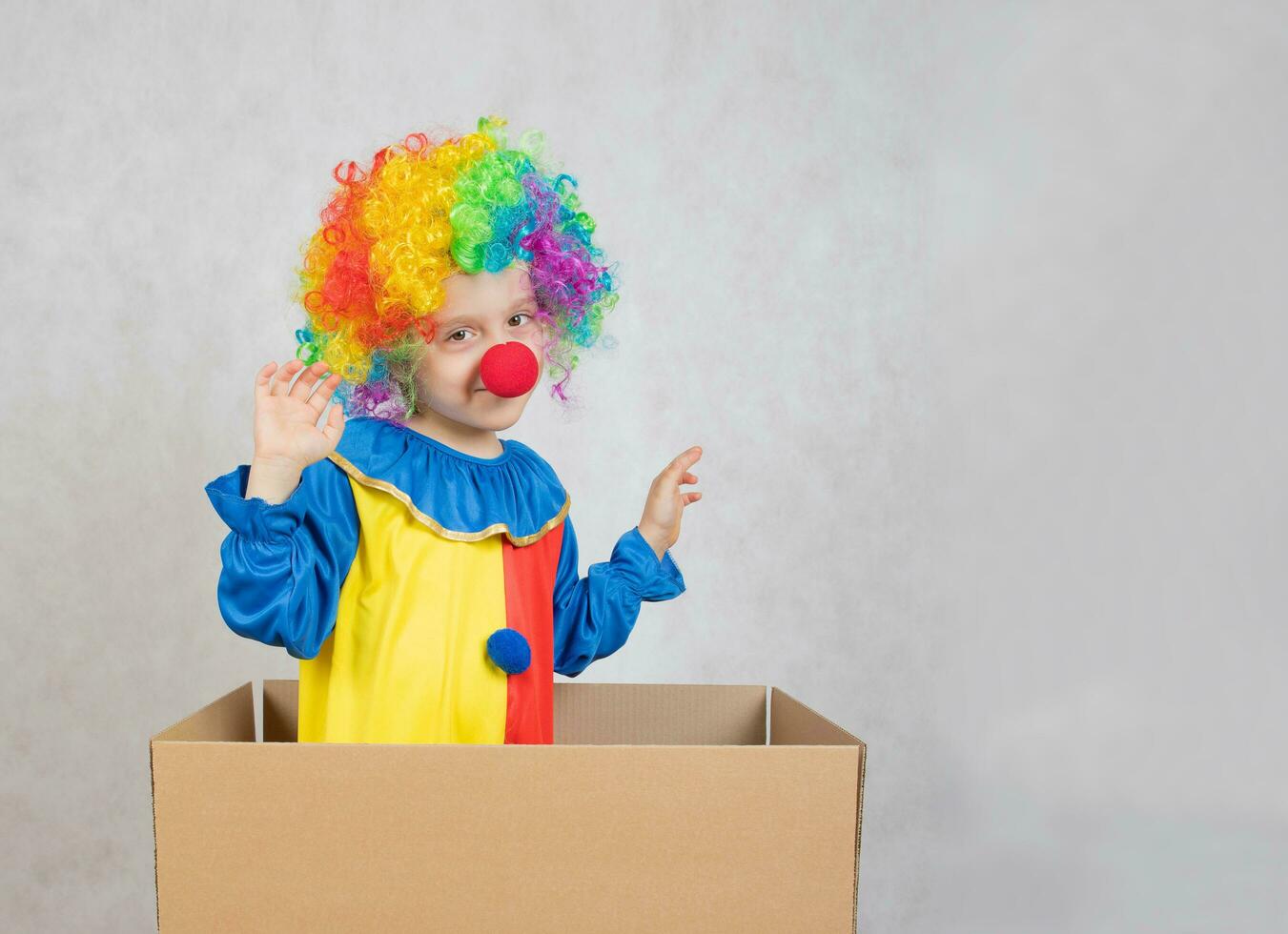 Boy of five years dressed in the costume of a clown stays in a carton paper box. photo