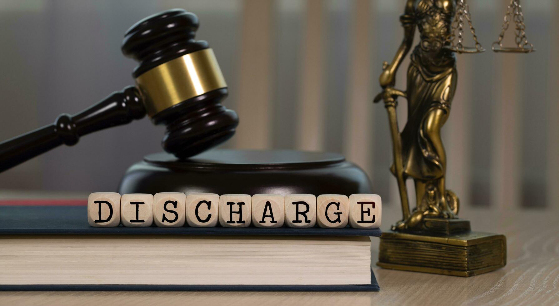 Word DISCHARGE composed of wooden dices. Wooden gavel and statue of Themis in the background. photo