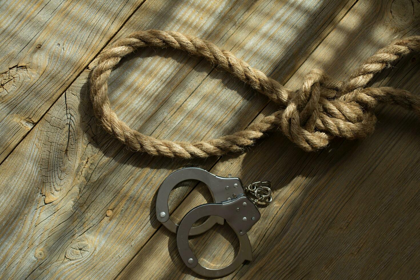 Rope with knot and handcuffs on a wooden surface. photo