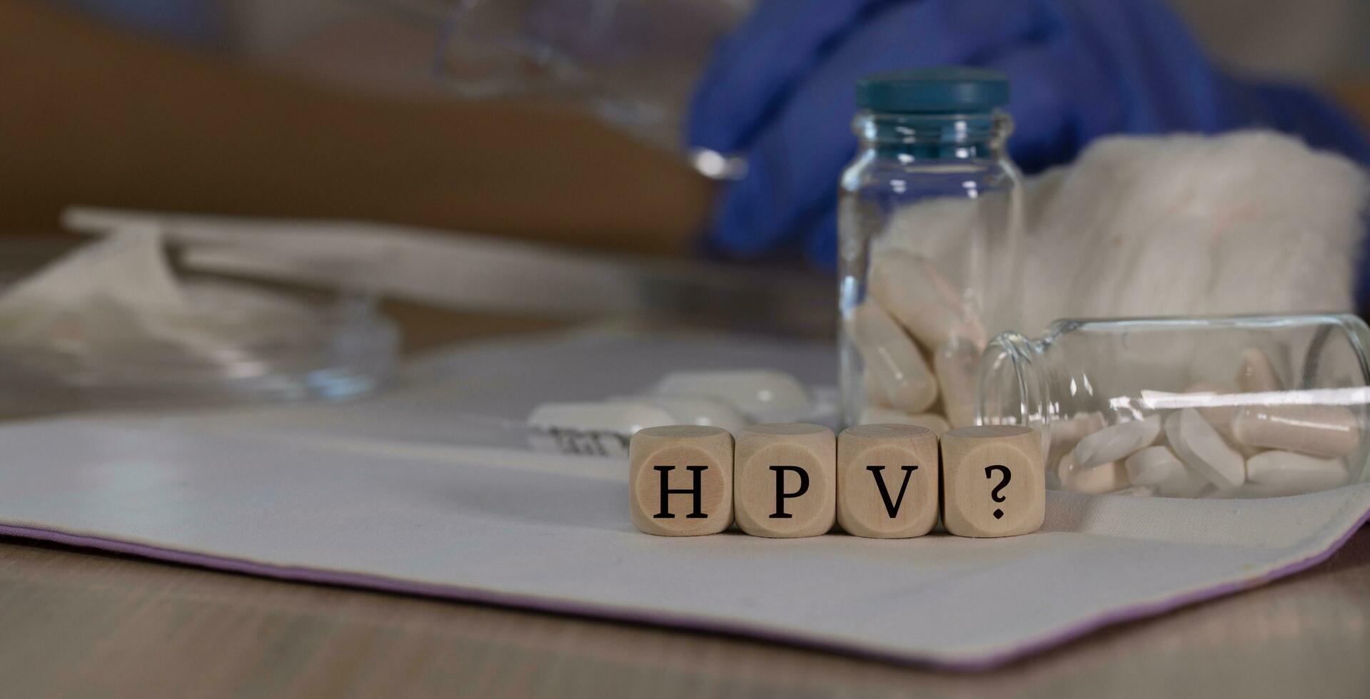 Abbreviation HPV with question mark for human papilloma virus infection composed of wooden dices. Pills, documents and a pen in the background. photo