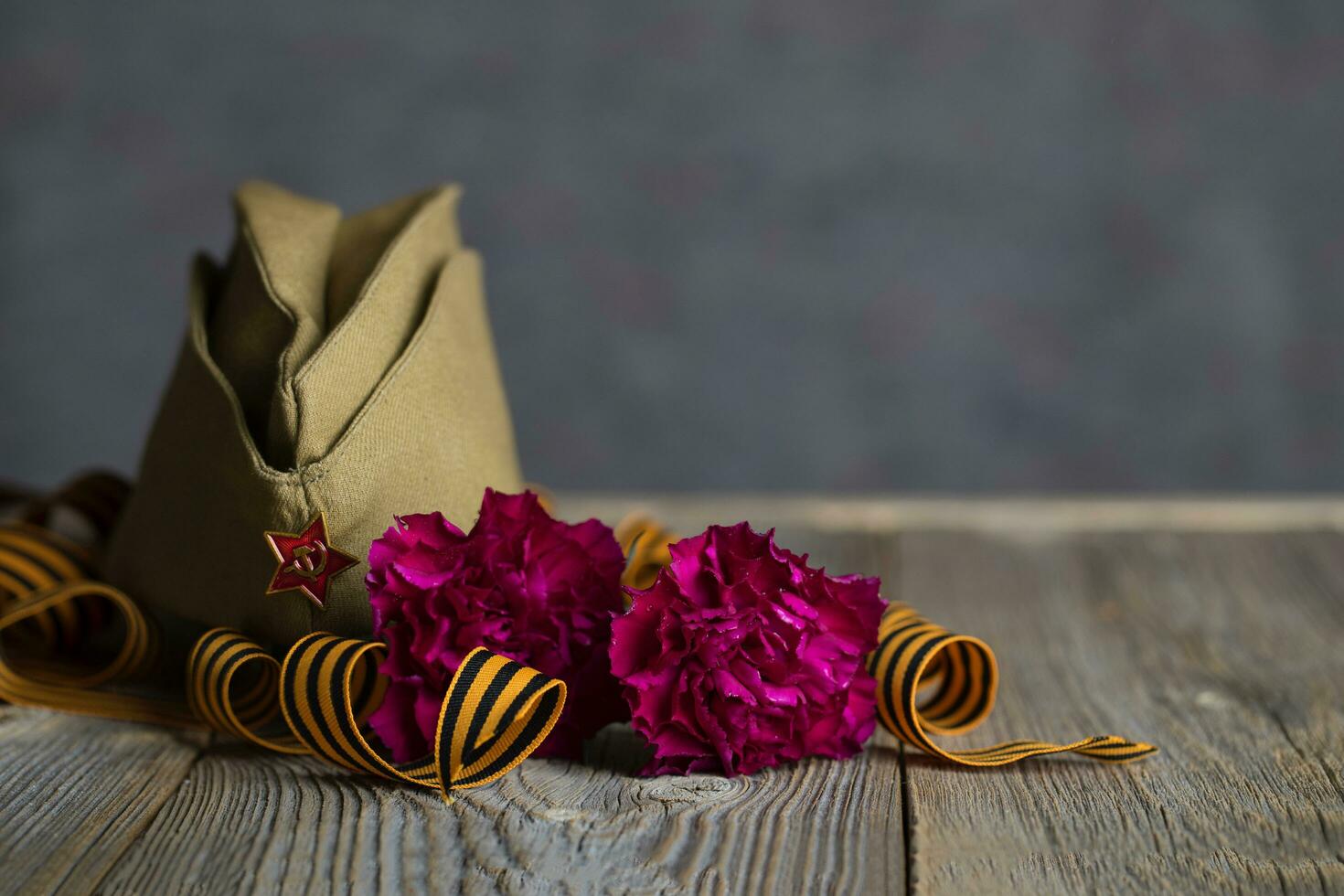 Military cap, carnations, Saint George ribbon on a wooden surface. photo