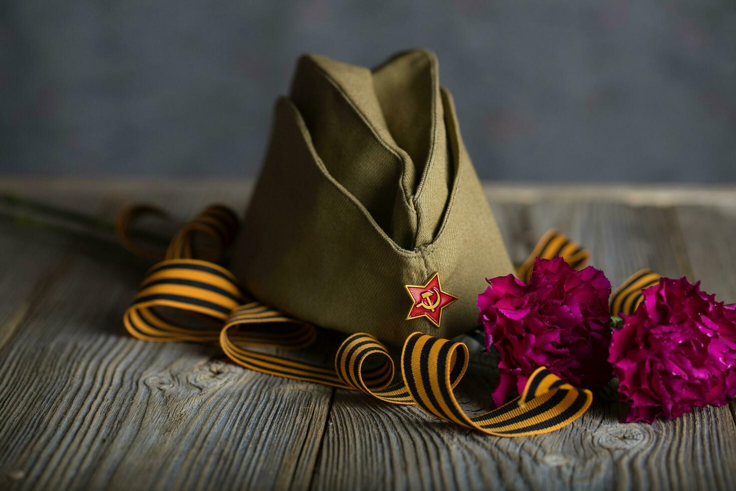 Military cap, carnations, Saint George ribbon on a wooden surface. photo