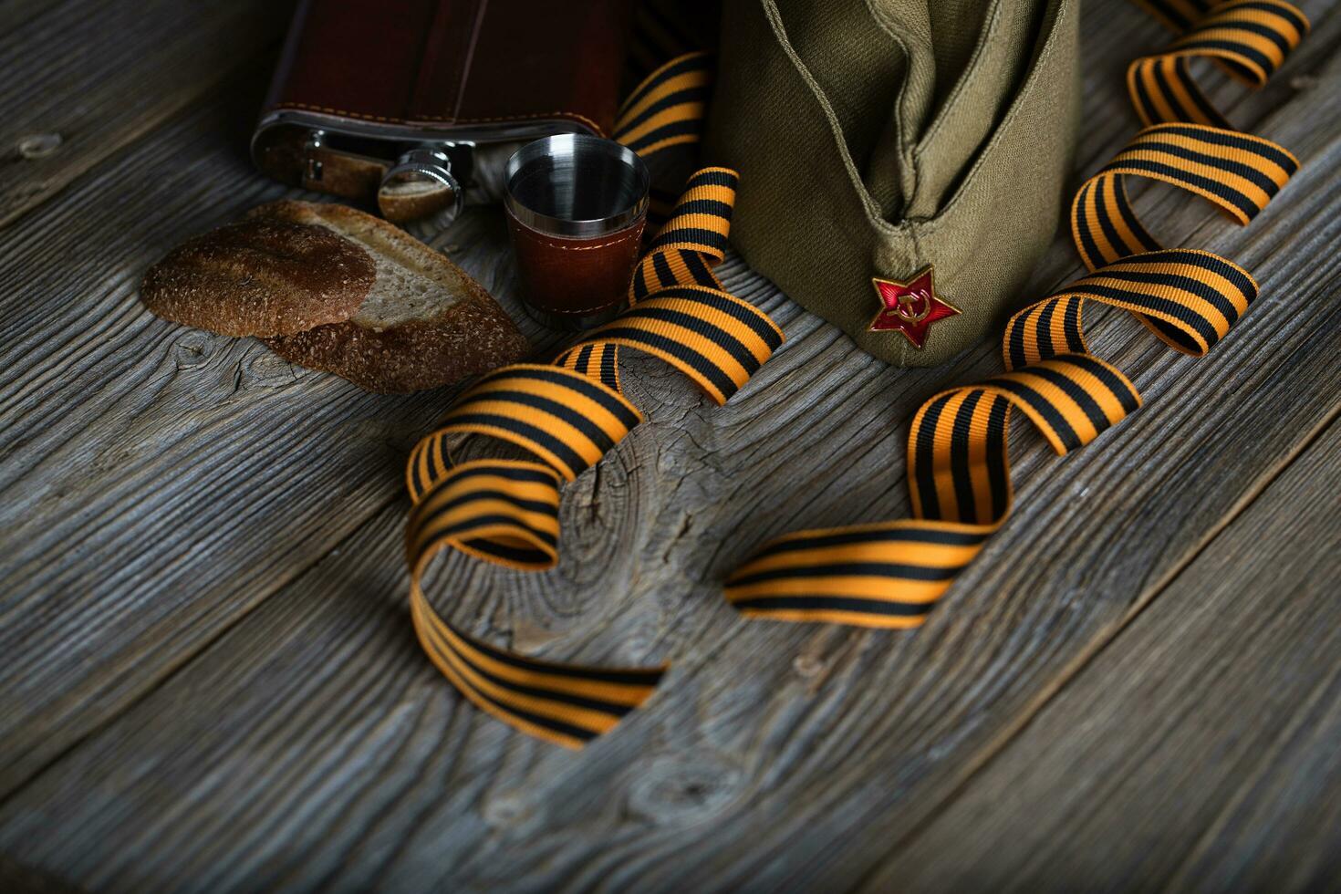 Military cap, carnations, Saint George ribbons, flask with alcohol  on a wooden surface. photo