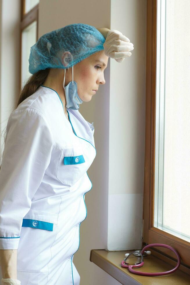 Young surgeon after a working day stays close to the window in the clinic corridor photo