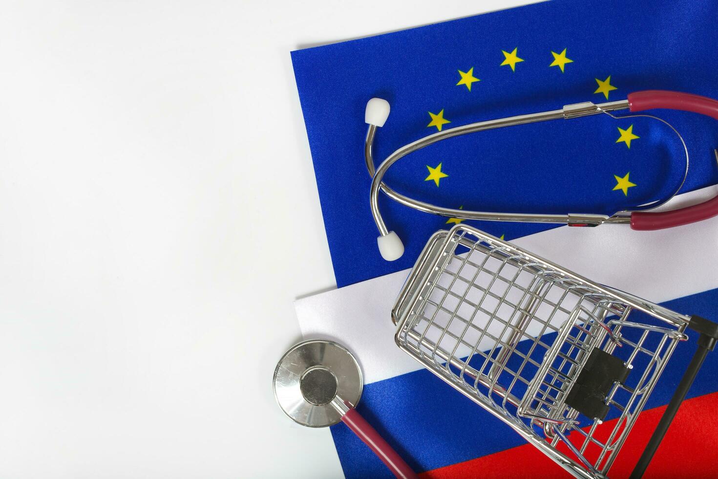 Shopping cart and stethoscope on European and Russian flags photo