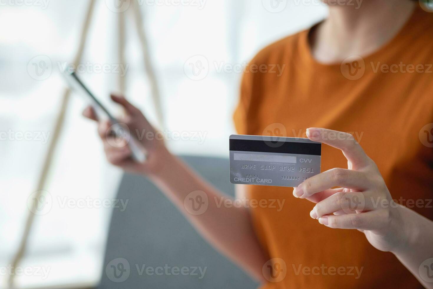 Young adult Asian female consumer holding credit card and smartphone sitting on the floor at home doing online banking transactions. E-commerce virtual shopping, secure mobile banking concept. photo