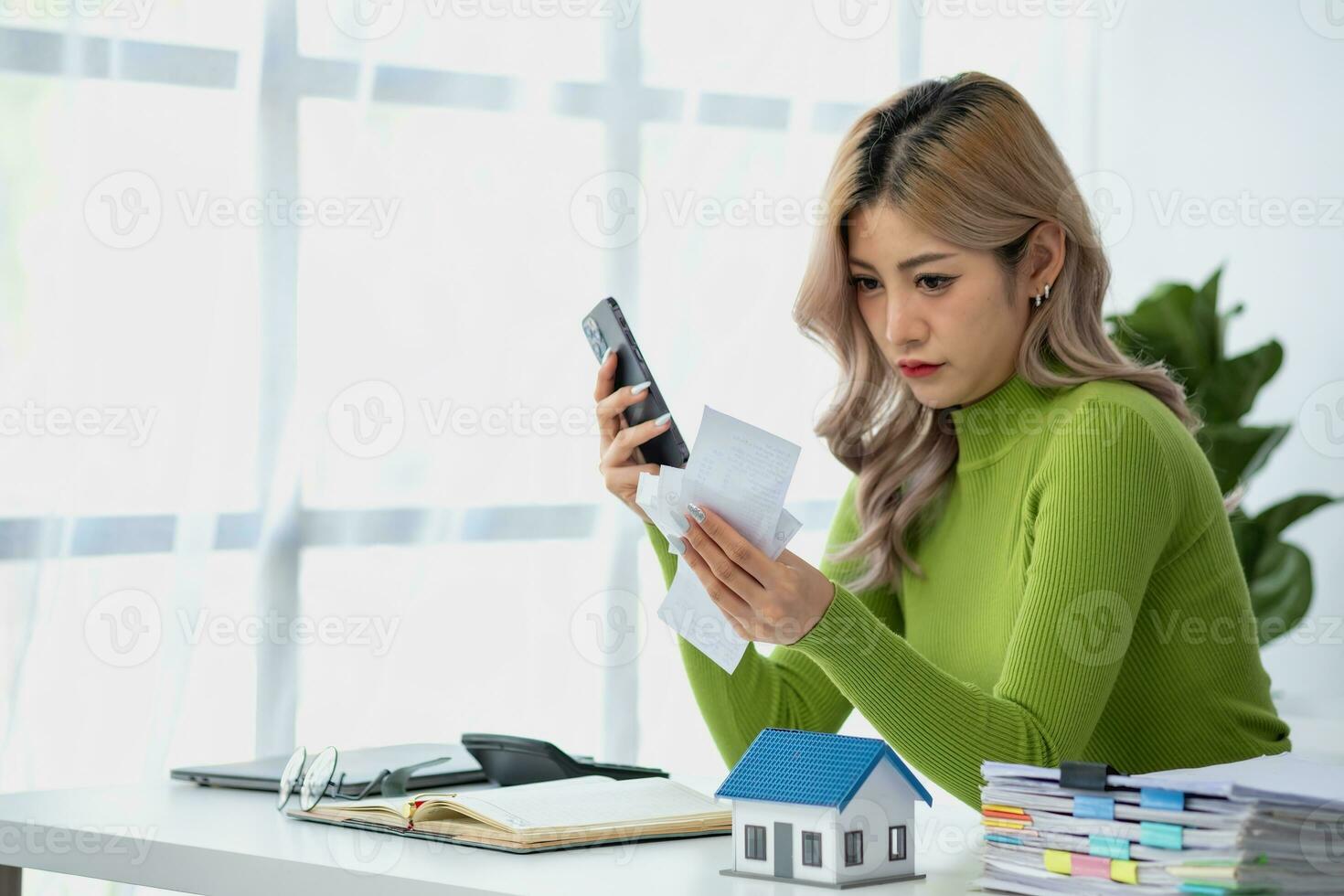 Young Asian woman sitting and calculating expenses and mortgage with calculator and house on table Worried about payments and non-repayable loans, business, and property. photo
