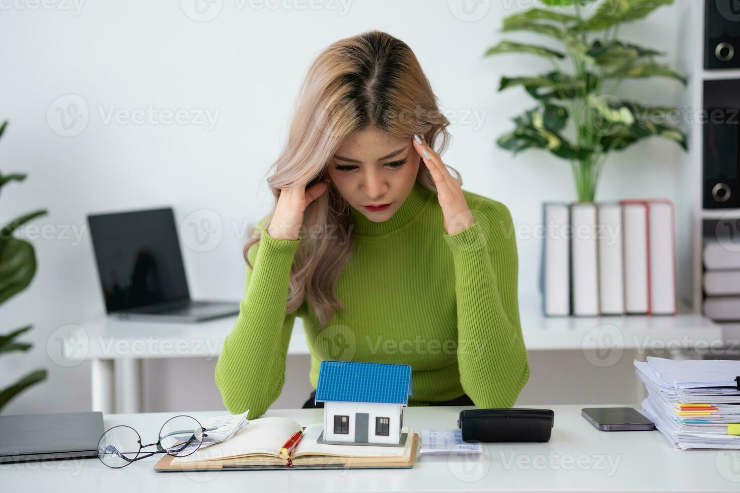 oung Asian woman sitting and calculating expenses and mortgage with calculator and house on table Worried about payments and non-repayable loans, business, and property photo