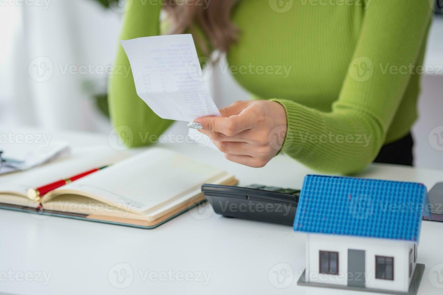 oung Asian woman sitting and calculating expenses and mortgage with calculator and house on table Worried about payments and non-repayable loans, business, and property photo