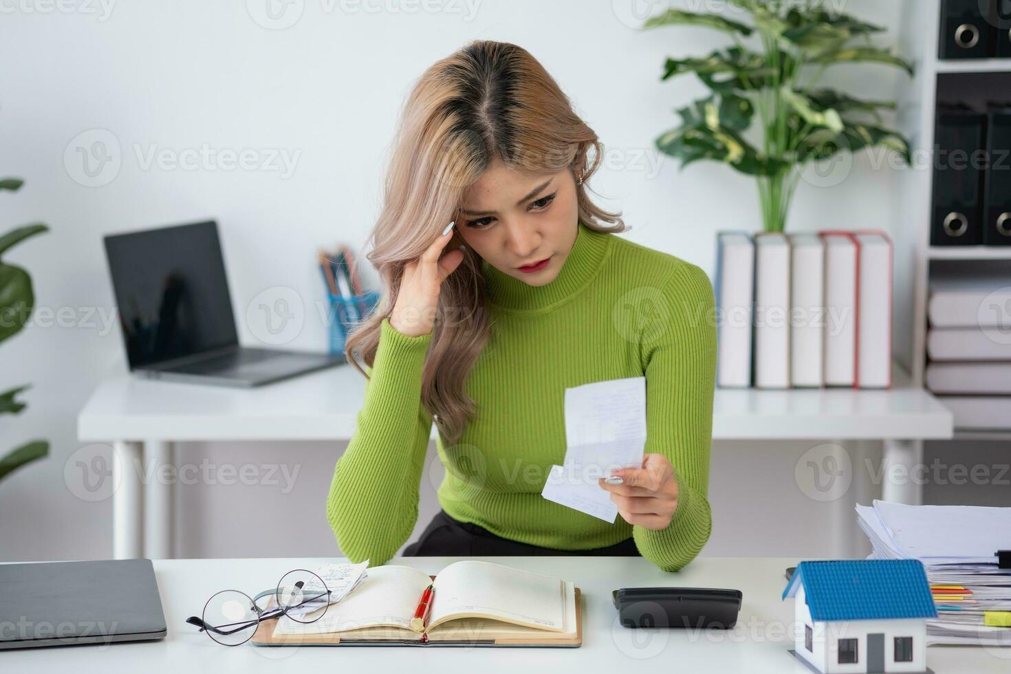 oung Asian woman sitting and calculating expenses and mortgage with calculator and house on table Worried about payments and non-repayable loans, business, and property photo