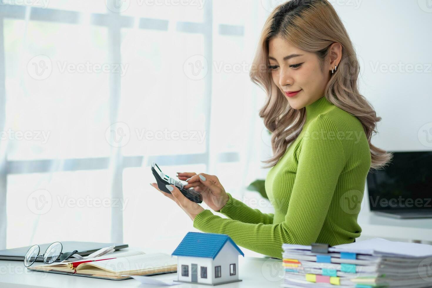 woman sitting on cozy sofa and planning and calculate expense and mortgage with calculator and home on desk, insurance and budget of residential, loan and residence, business and property concept. photo