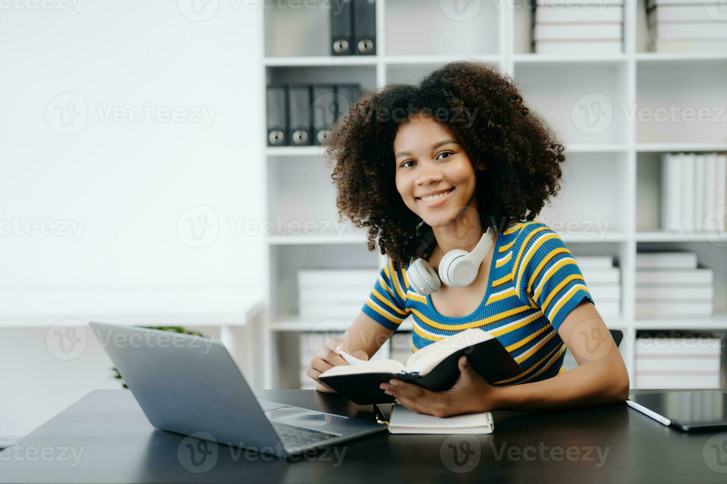 Female students note from the books at the African girl library sitting at the desk using laptop computer and tablet to search an online informations. photo