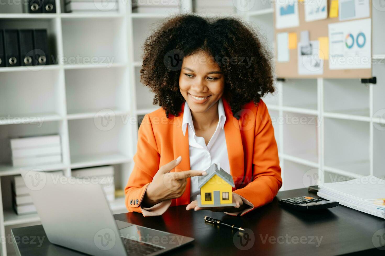 Young real estate agent worker working with laptop and tablet at table in office and small house beside it. photo