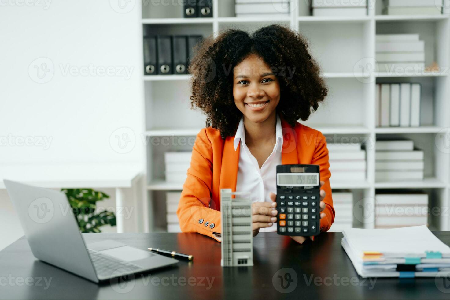 Young real estate agent worker working with laptop and tablet at table in office and small house beside it. photo