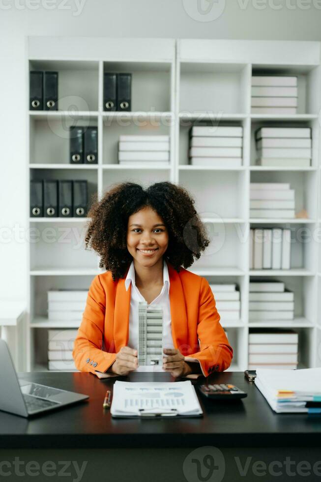 Young real estate agent worker working with laptop and tablet at table in office and small house beside it. photo