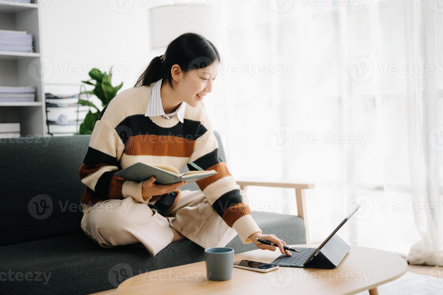 Confident Asian woman with a smile standing holding notepad and tablet in living room on the sofa at home photo