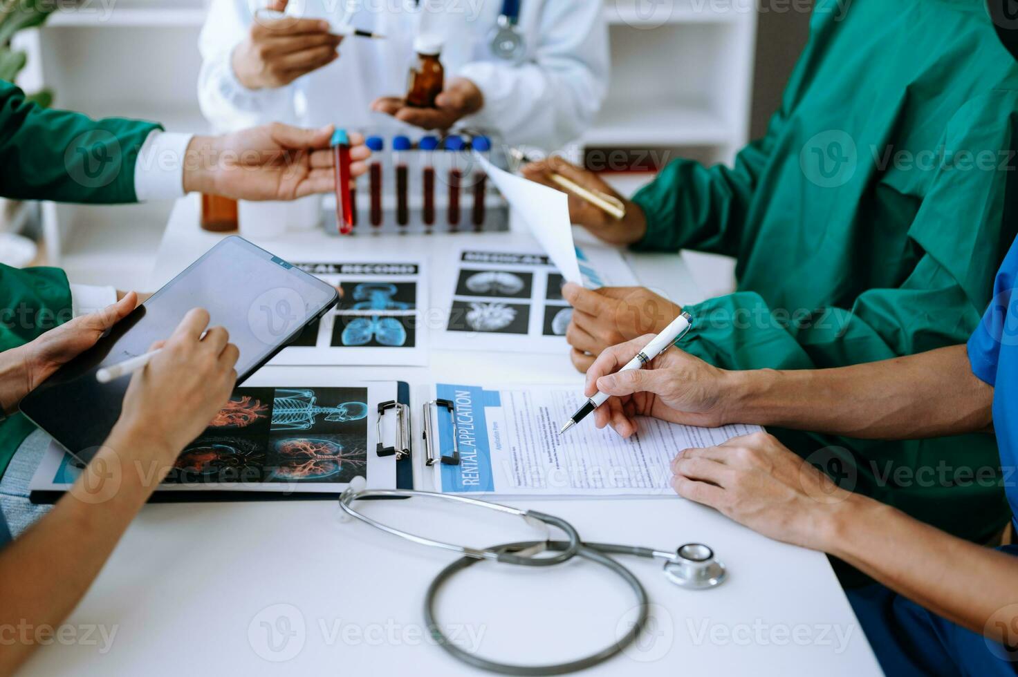 Medical team having a meeting with doctors in white lab coats and surgical scrubs seated at a table discussing a patients working online using computers photo
