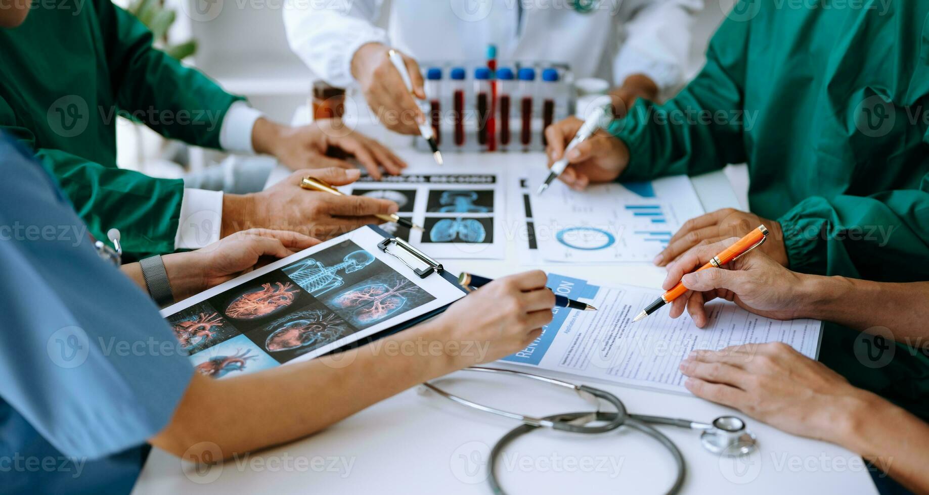 Medical team having a meeting with doctors in white lab coats and surgical scrubs seated at a table discussing a patients working online using computers photo