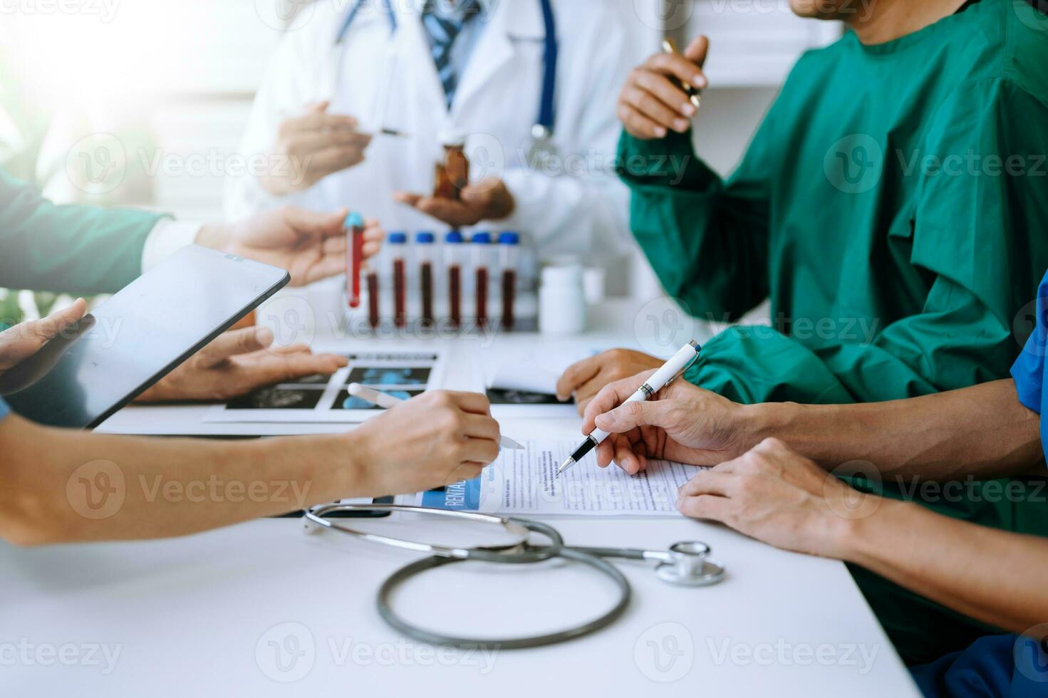 Medical team having a meeting with doctors in white lab coats and surgical scrubs seated at a table discussing a patients working online using computers photo