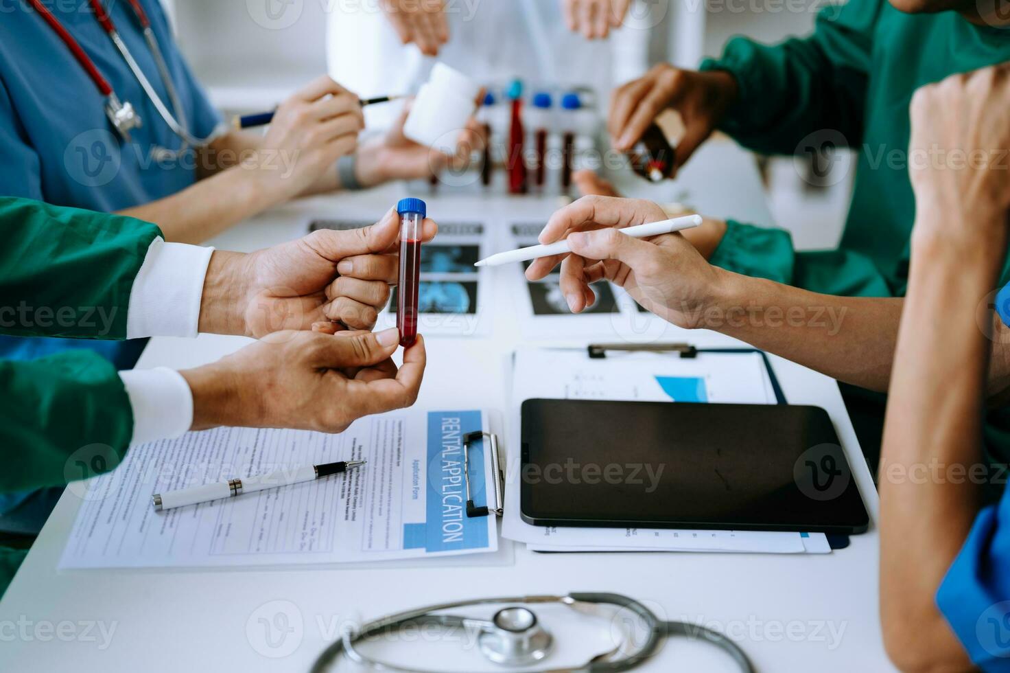 Medical team having a meeting with doctors in white lab coats and surgical scrubs seated at a table discussing a patients working online using computers photo