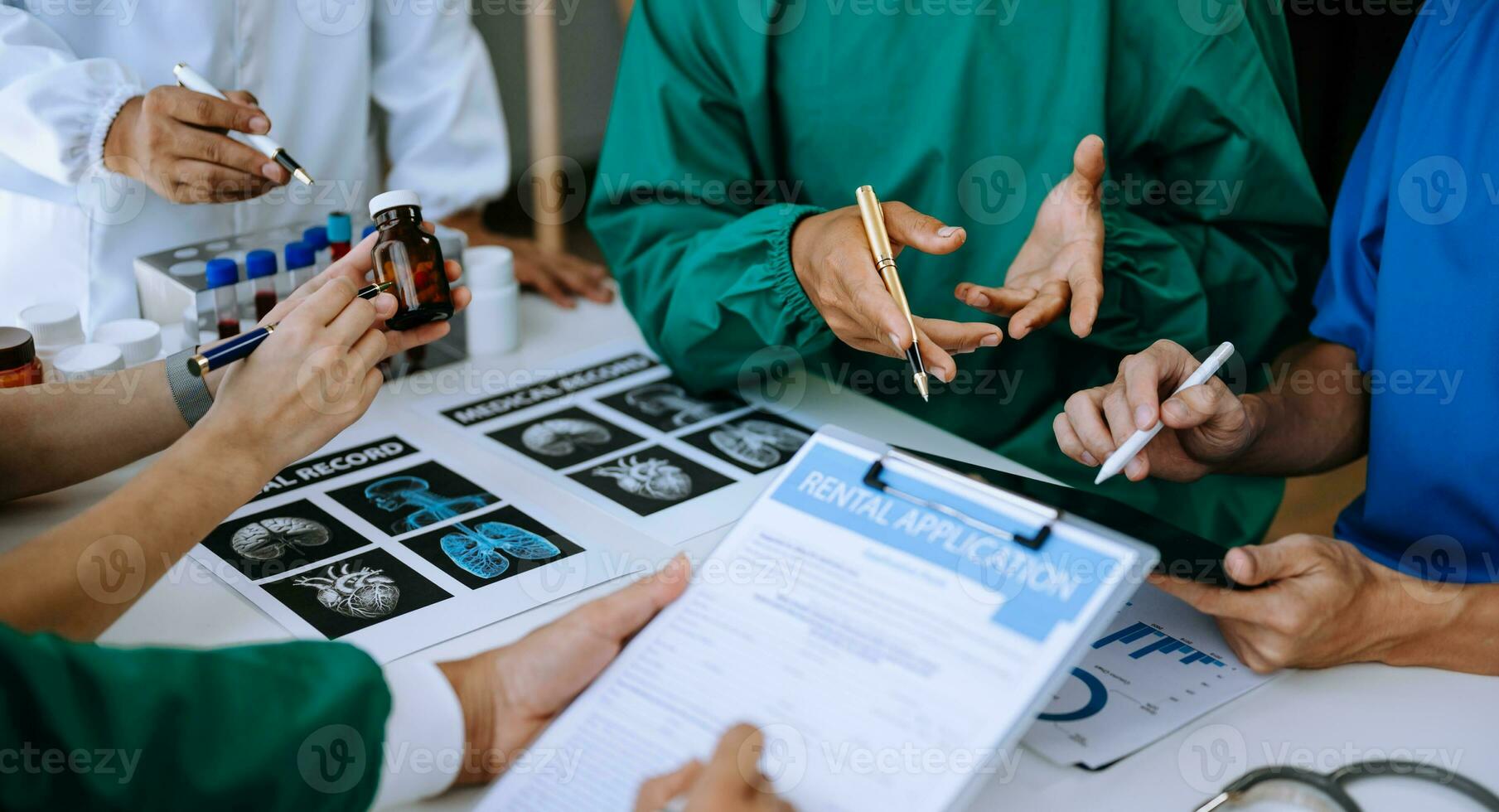 Medical team having a meeting with doctors in white lab coats and surgical scrubs seated at a table discussing a patients working online using computers photo