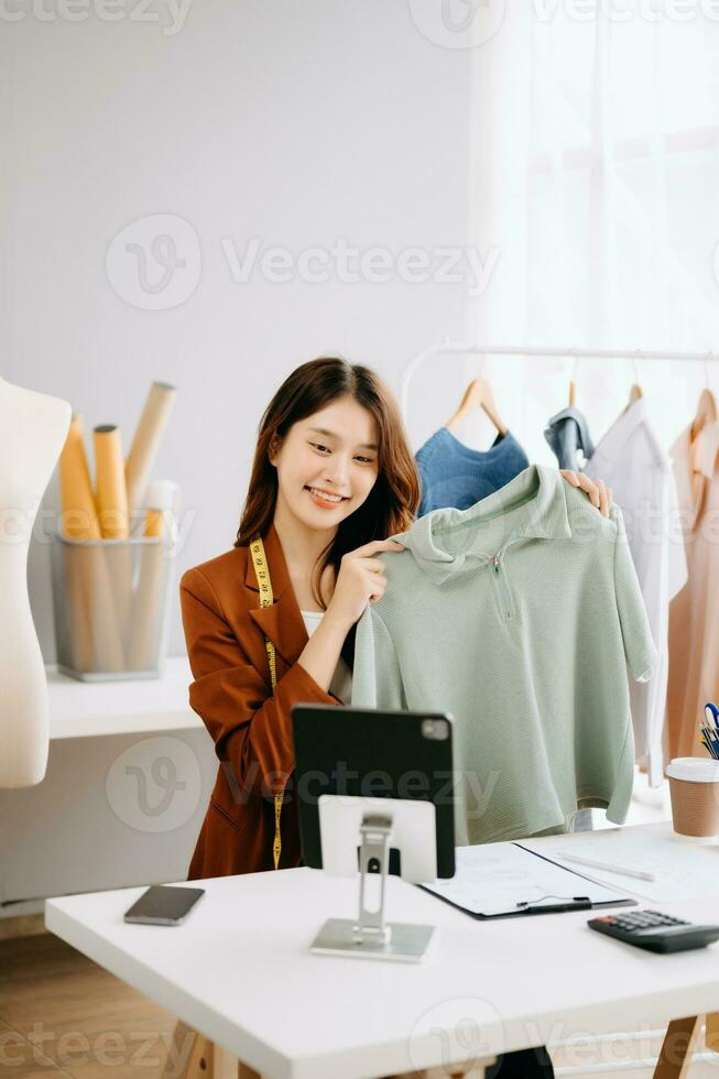 Fashion blogger concept, Young Asian women selling clothes on video streaming.Startup small business SME, using smartphone or tablet taking receive and checking photo