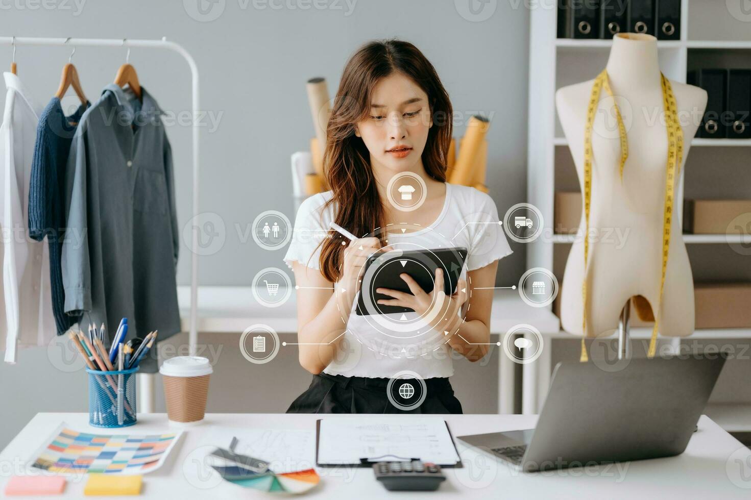 Asian young woman on desk in office of fashion designer and holds tablet, laptop and smartphone on white table photo