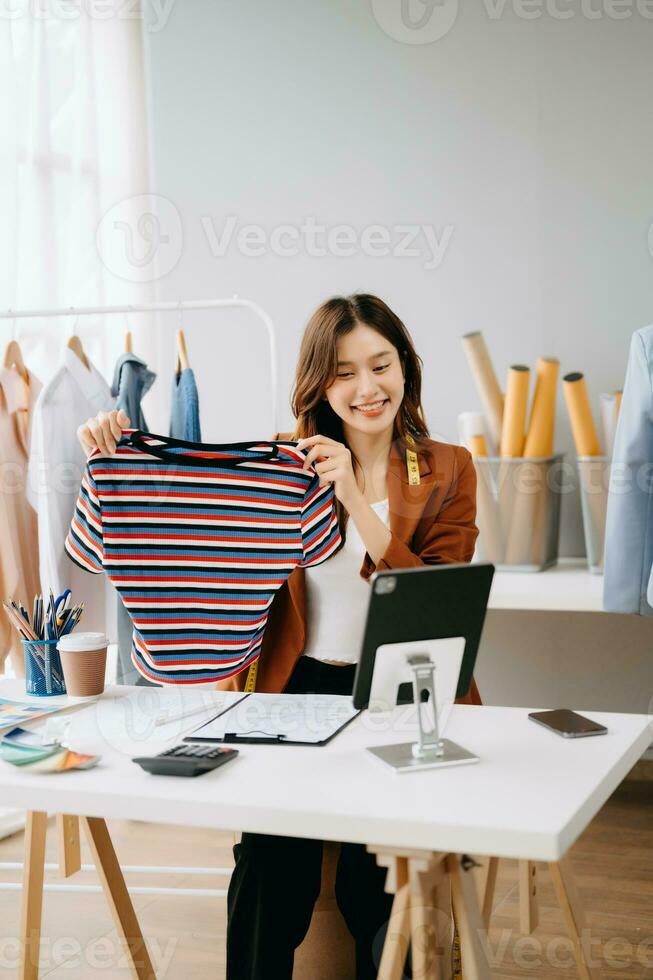 Fashion blogger concept, Young Asian women selling clothes on video streaming.Startup small business SME, using smartphone or tablet taking receive and checking photo