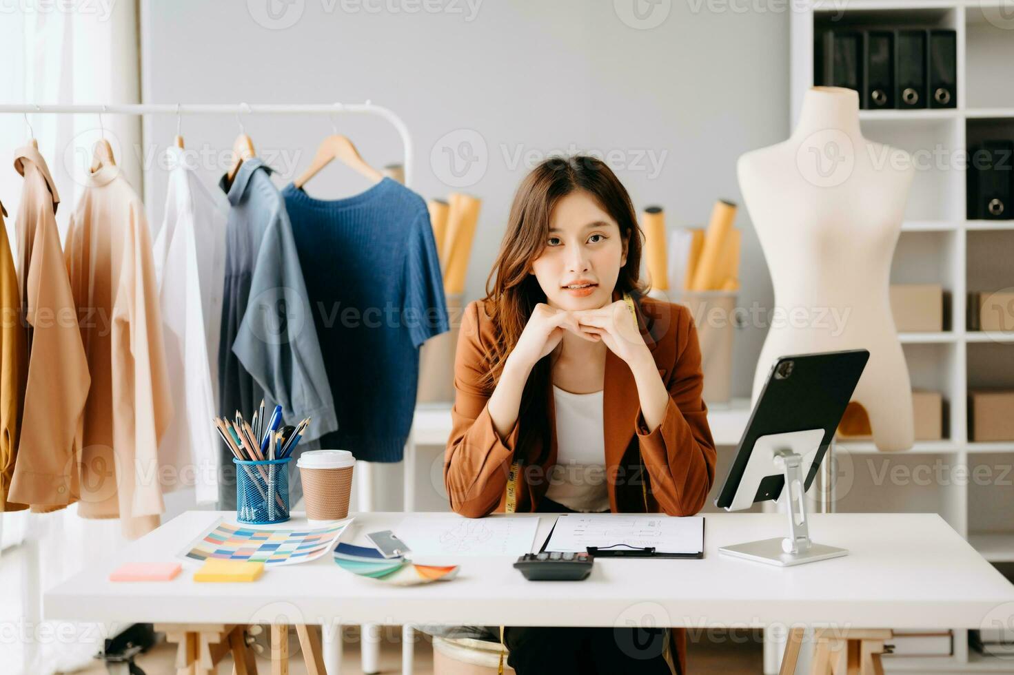 Asian tailor woman working on clothes in tailoring atelier.  beautiful young female fashion designer smile and after success in studio photo