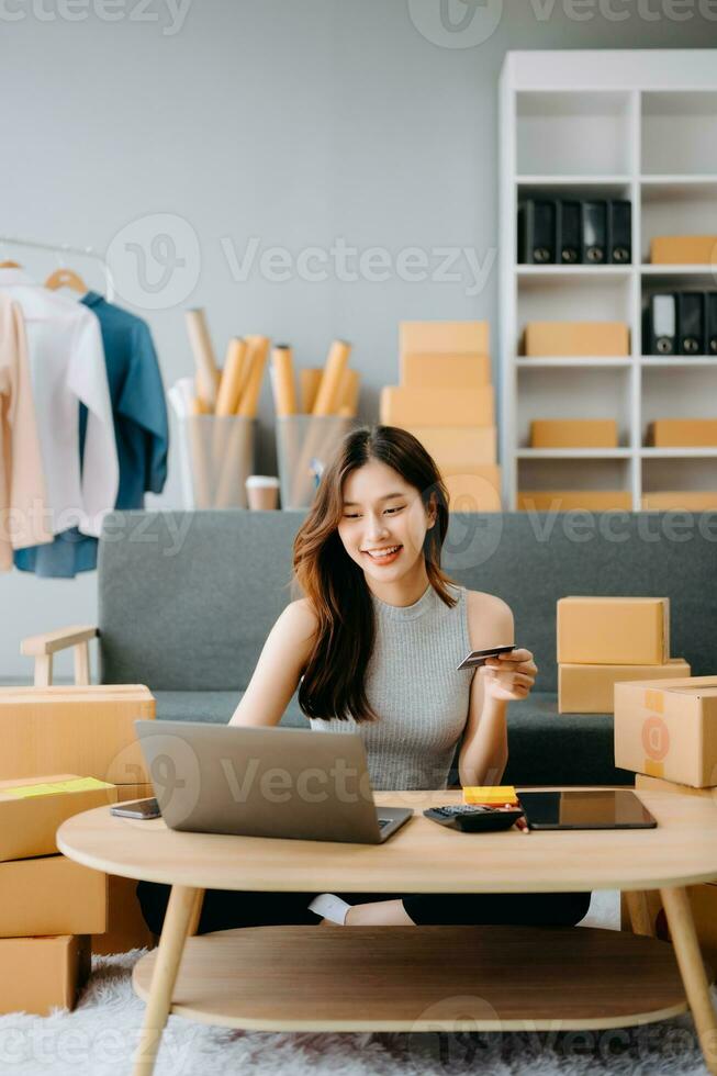 Startup small business SME, Entrepreneur owner woman using smartphone or tablet taking receive and checking online purchase shopping order to preparing pack product box. photo