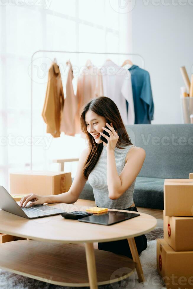 Startup small business SME, Entrepreneur owner woman using smartphone or tablet taking receive and checking online purchase shopping order to preparing pack product box. photo