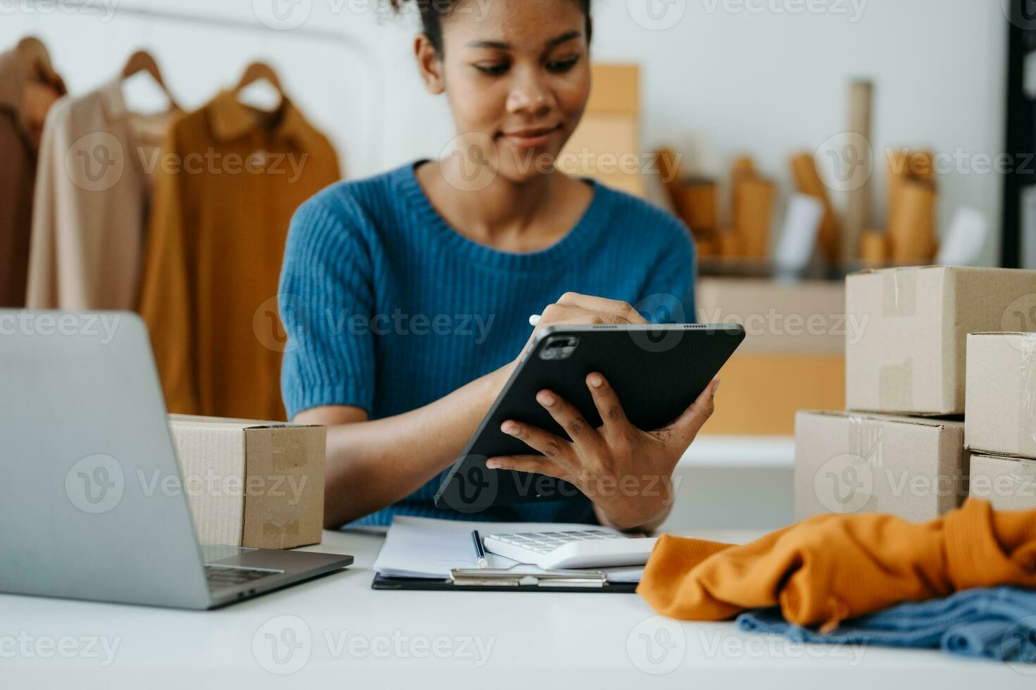 Startup small business SME, Entrepreneur owner woman using smartphone or tablet taking receive and checking online purchase shopping order to preparing pack product box. in office photo