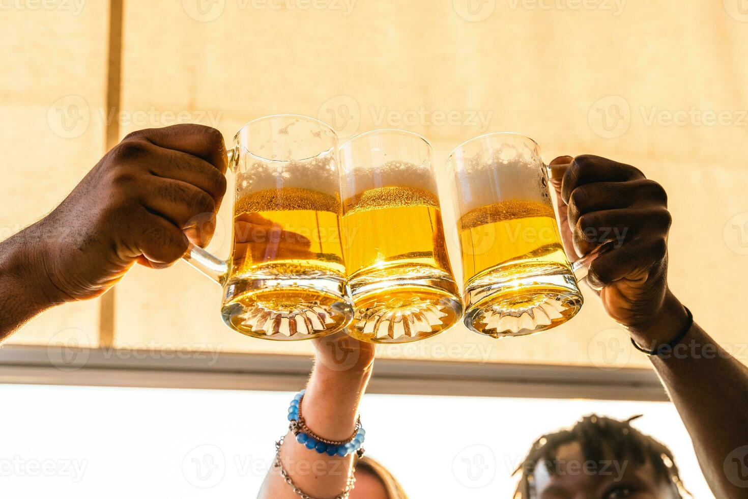 pequeño grupo de joven adulto multiétnico amigos tostado con Tres tazas de cerveza foto