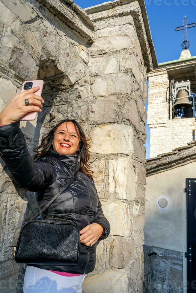 middle aged woman wearing winter clothes taking a selfie over a mountain photo